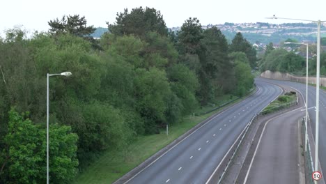 empty dual carriageway road in early morning with houses on tree covered hills in background