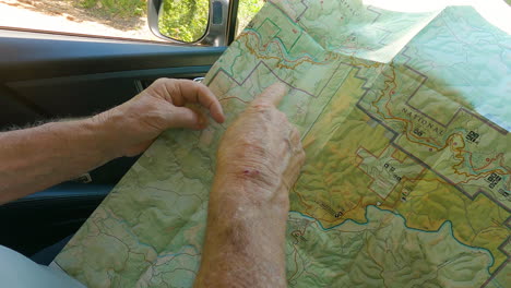 senior hiker planning route on paper map, pov