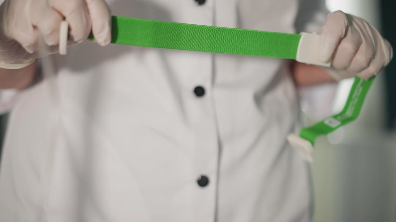 Infermiera applica il laccio emostatico. Procedura di posizionamento della fascia sterile. Posizionamento e ispezione accurati del laccio emostatico da parte dell'infermiera. L'infermiera della clinica prepara e verifica meticolosamente il laccio emostatico verde con attenzione.