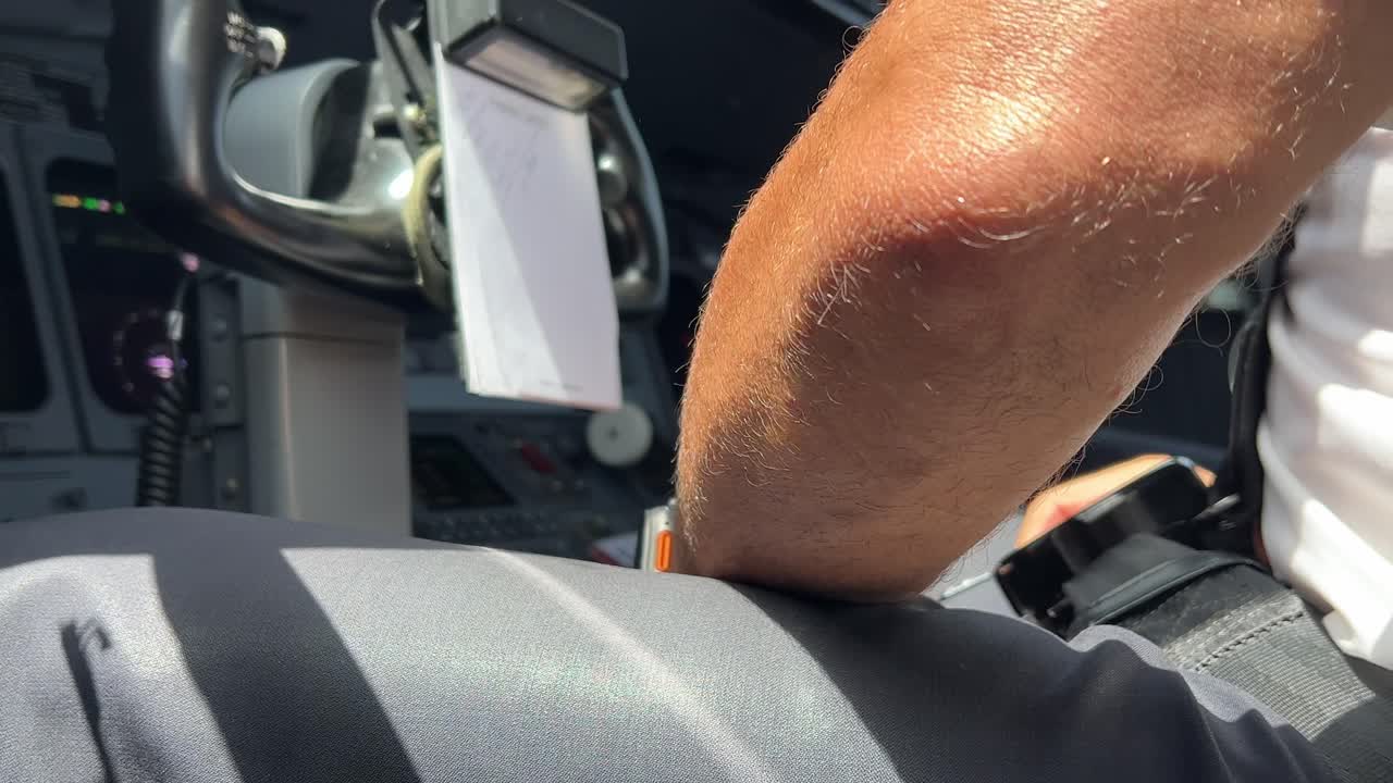 현대적 인 제트 항공기 객실 내 에서 이륙 하기 전 에 조종사 가 장비 와 베일트 를 조정 하는 모습 을 가까이서, 낮은 각도 에서 볼 수 있다