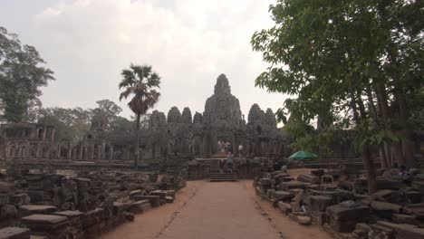 Tourists-walking-toward-the-entrance-of-ancient-Bayon-temple-in-Angkor-complex,-point-of-view-POV