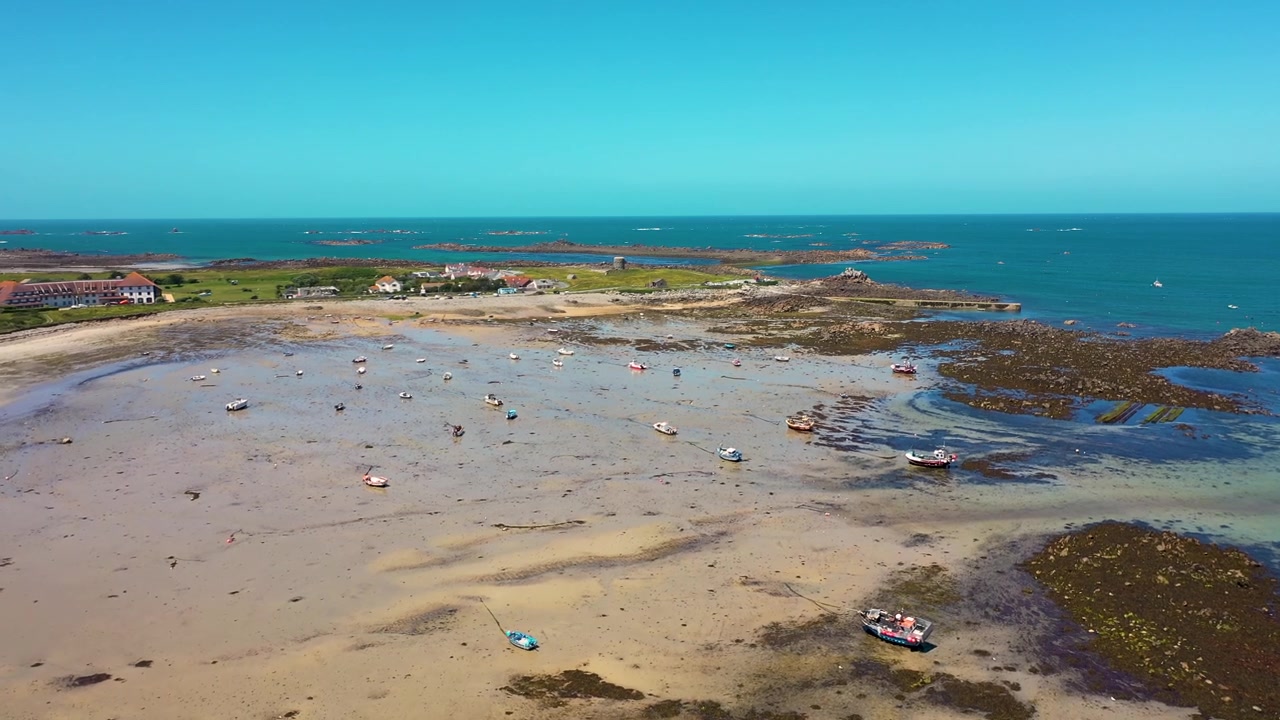 Flight over north Guernsey natural bay with drying boats on a summer day with sandy beach and Martello Tower and sea in the background