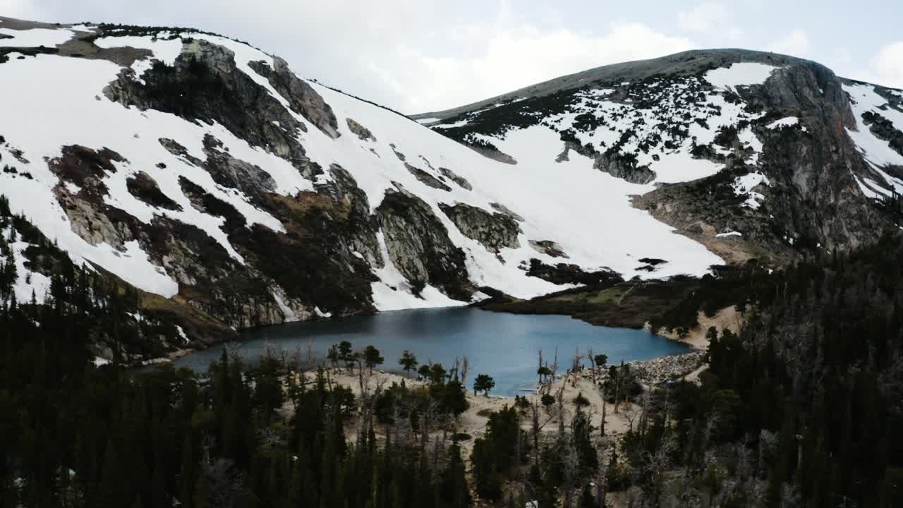Drone shot pushing towards the isolated Saint Mary's Lake lying beneath a semi-permanent snowfield in Colorado