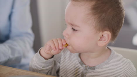 Unerkennbare-Mutter,-Die-Ihren-Kleinen-Sohn-Mit-Clementinenstücken-Füttert,-Während-Sie-Zu-Hause-Zusammen-Am-Tisch-Sitzt