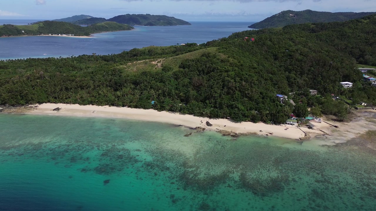 Filipinler’in Romblon bölgesindeki Tiamban Plajı’nın turkuaz okyanusunu, beyaz kumlu kıyı şeridini ve arka plandaki yemyeşil tepelerini güneşli bir tropikal günde masmavi bir gökyüzünün altında gösteren sinematik bir kuşbakışı.