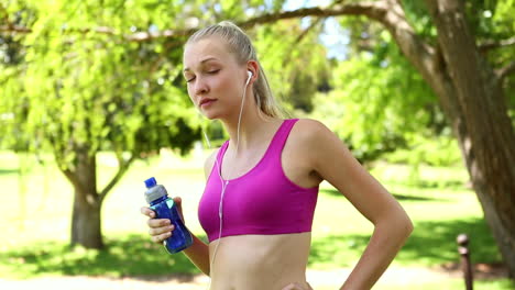 fit blonde drinking water in the park on her jog