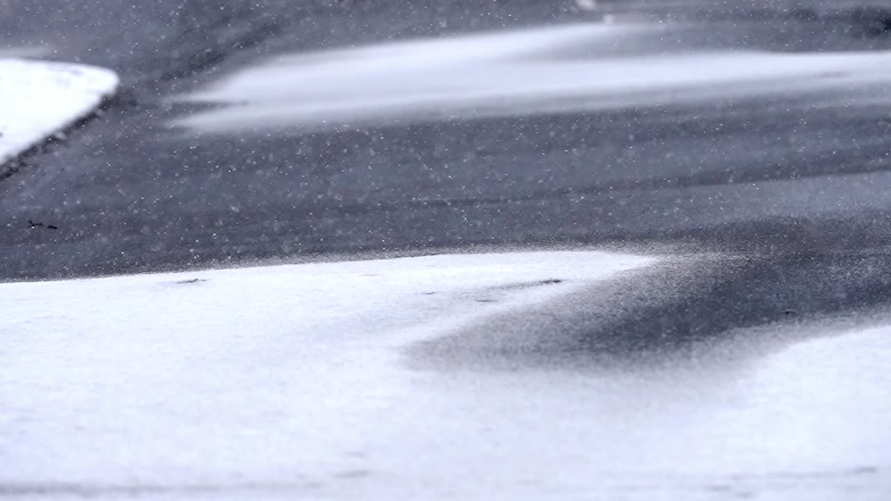 Light snowfall on snow covered asphalt, street, road, static shot of snowflakes falling in winter, copy space, background footage