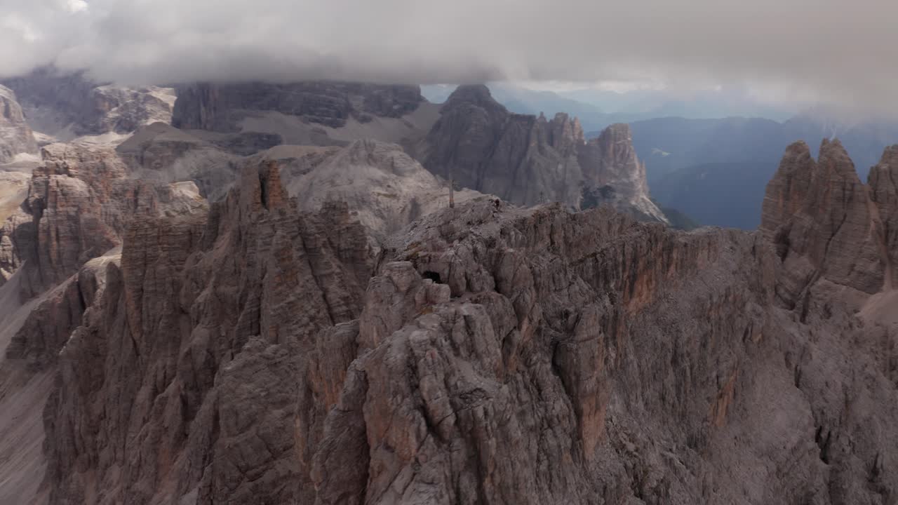 Aerial orbit shot around cross on peak of Tre Cime Di Lavaredo Mountains in Dolomites with dark cloudscape on top, South Tyrol