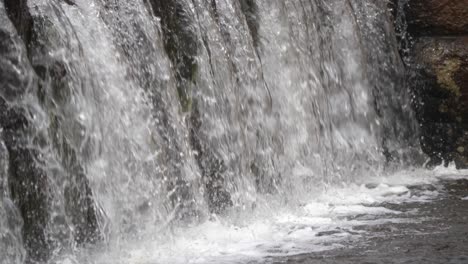 Closeup-of-a-man-made-waterfall-with-water-hitting-the-ground-below