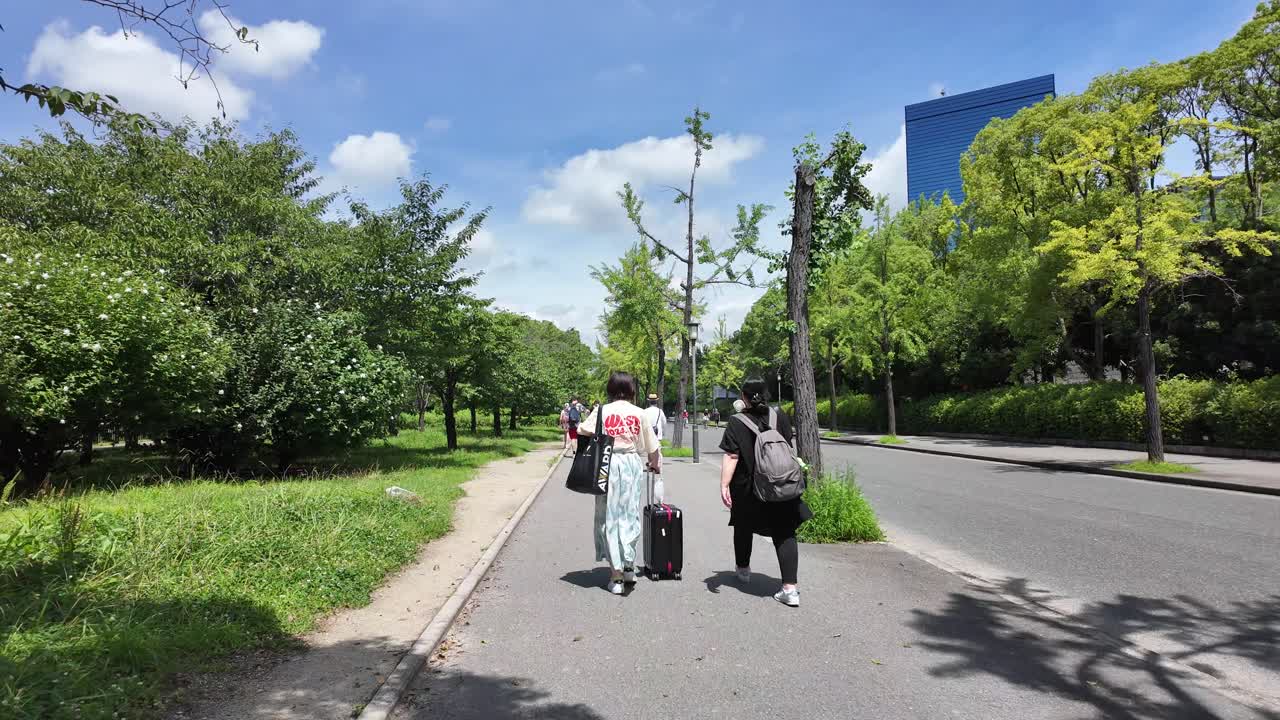 People walking on a tree-lined street with luggage and backpacks