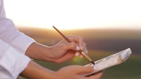 young girl artist who paints a picture of nature. - the girl stands with brushes in her hands and paints a picture. talented man in painting