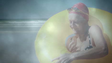 animation of glowing lights over senior woman with yellow inflatable ring by sea and clouds