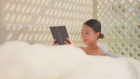 asian girl in bathtub relaxing and having a hygge moment in a bubble bath while reading a book