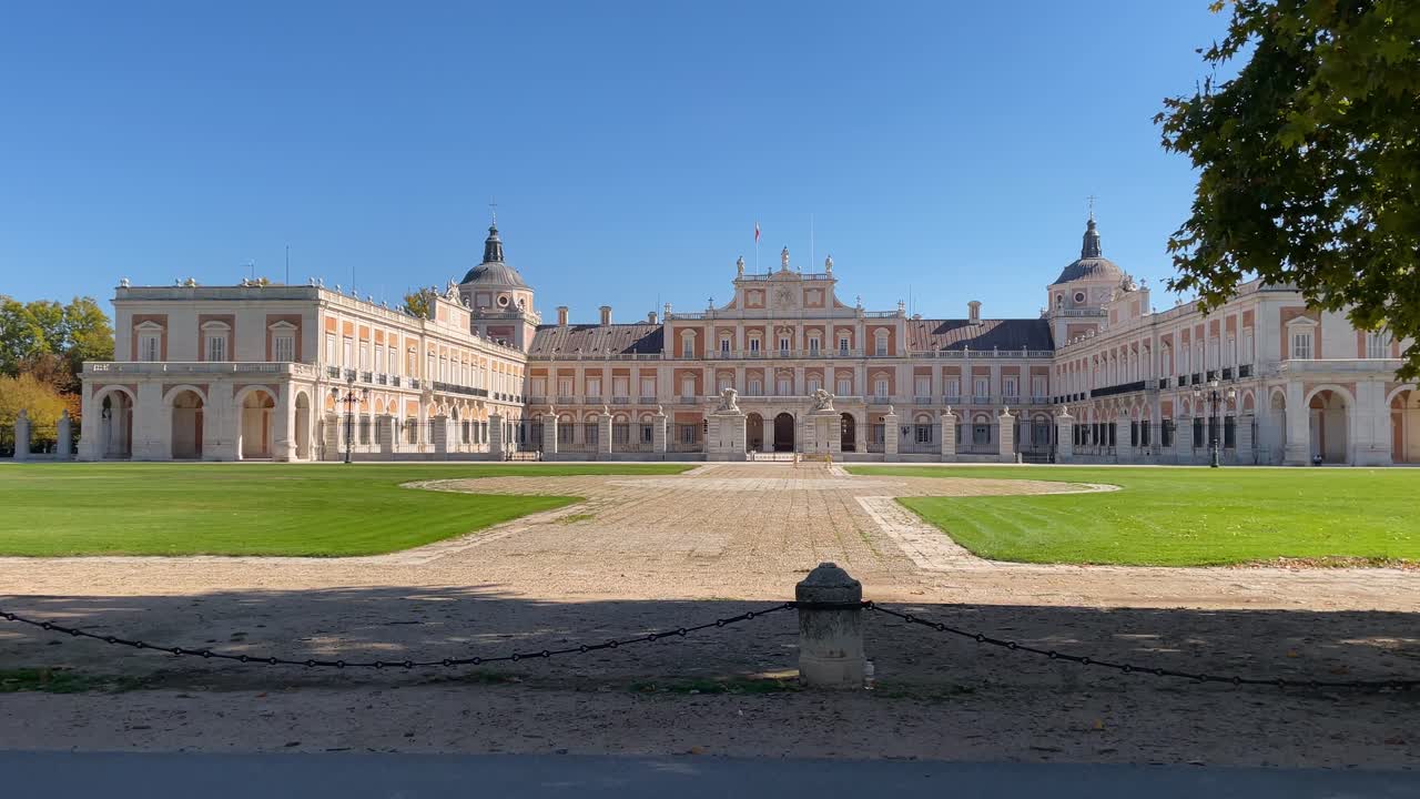 High-quality filming of the facade and main entrance of the magnificent Baroque-style Royal Palace of Aranjuez, where we appreciate its entrance and parade ground, with a blue sky background