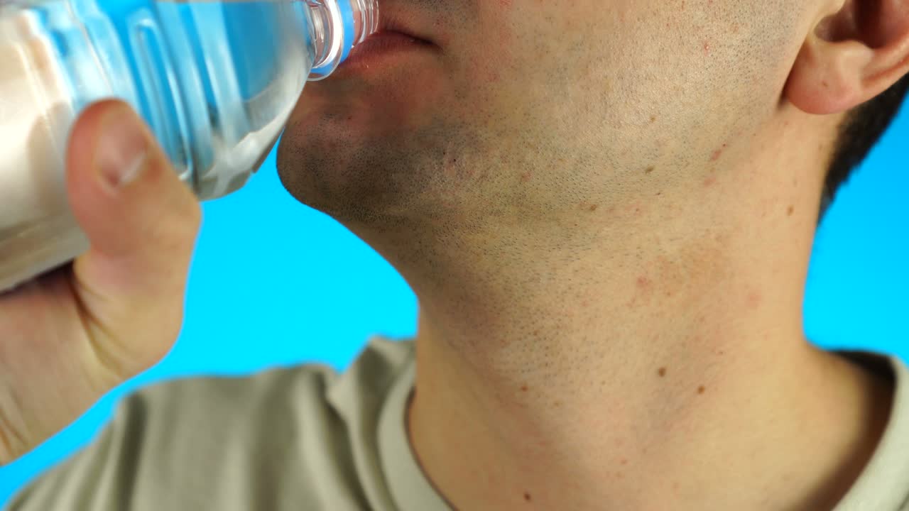 파란색 배경에 플라스틱 병에서 물을 마시는 젊은 남성. 클로즈업.