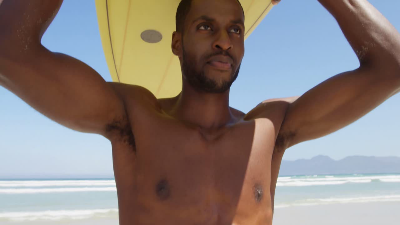 surfista masculino llevando una tabla de surf en su cabeza en la playa 4k