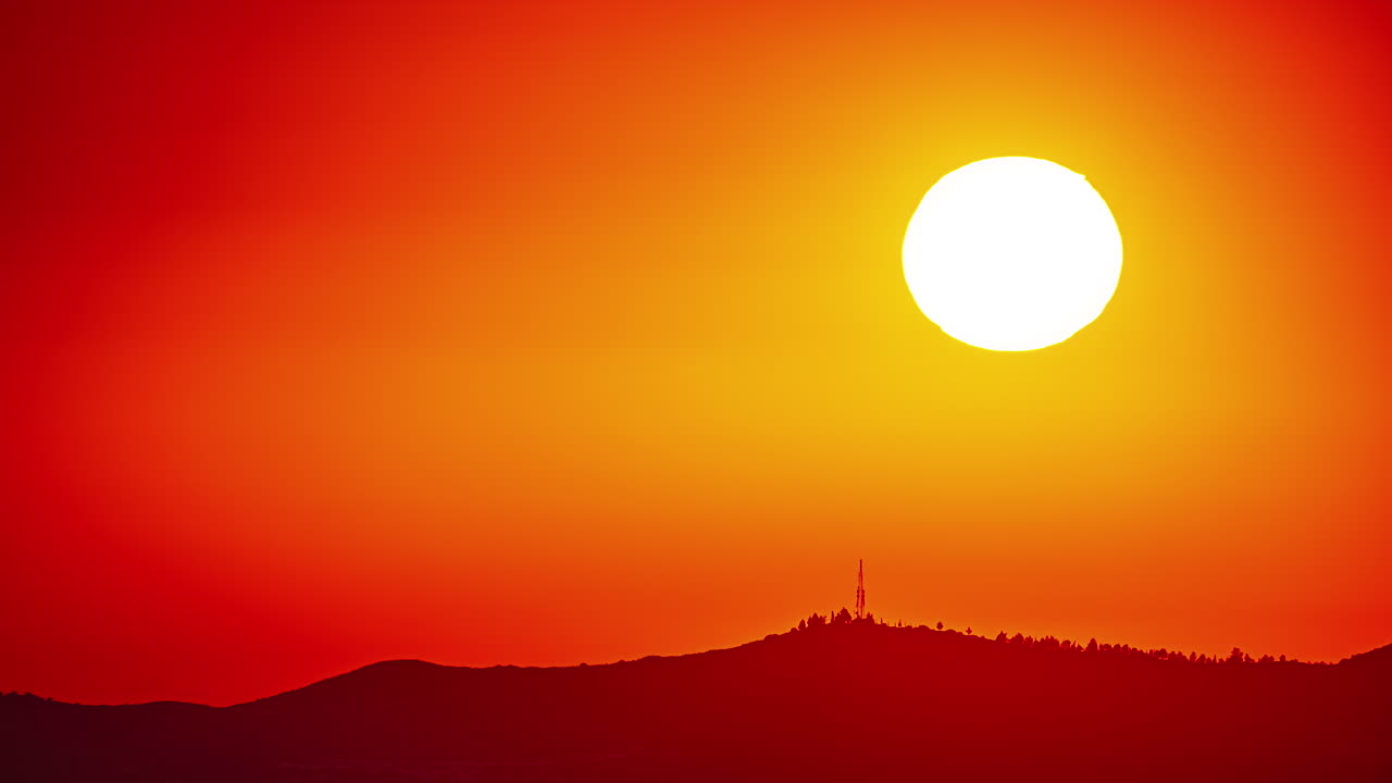 타임  ⁇ 스 거대한 태양이 불타는 하늘을 가로질러 움직이고 실루 ⁇  산 위에 자리 잡고 있습니다.