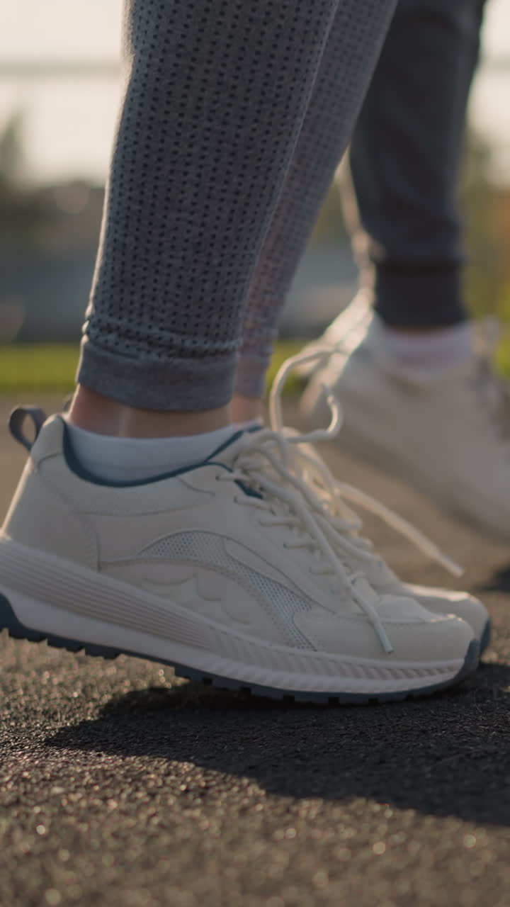 Vista lateral de personas en ropa deportiva y zapatillas de lona saltando y moviéndose de lado con la luz del sol reflejándose en ellas, con instalaciones deportivas visibles al fondo