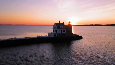 low and slow aerial slide past a backlit lighthouse at the end of a breakwater revealing the bright sunrise behind it