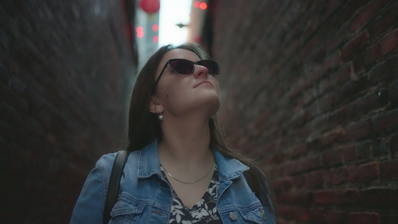 Close up of a woman with sunglasses looking up while walking in the narrow alley