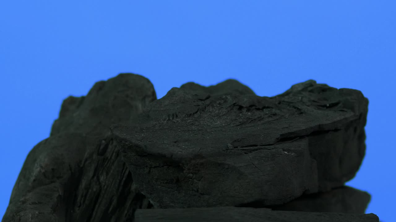 carbón de madera. madera natural o carbón negro tradicional en bucle en giratorio. fondo de pantalla azul o verde con luz led de color. disparo en estática. carbón para cocinar en la parrilla de la barbacoa. carbón negro.