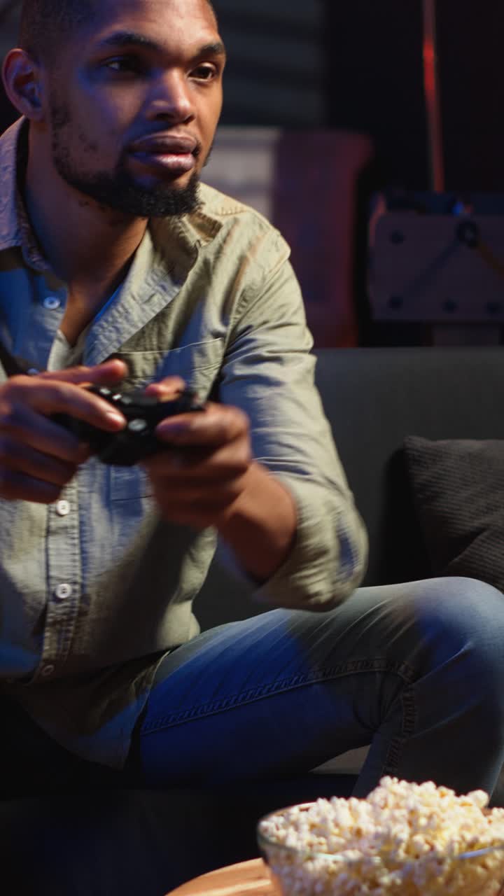 Video verticale: Gamer maschio che mangia popcorn mentre gioca a un torneo di sparatutto online.