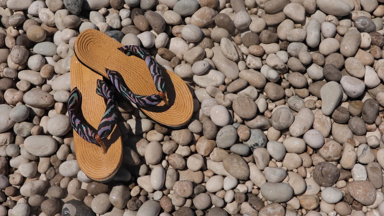 chanclas en la playa de guijarros bañada por agua de mar cristalina y espuma, concepto de viaje