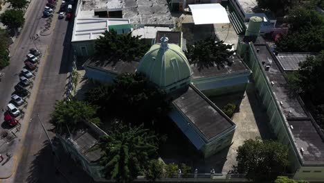 Aerial-camera-ascending-from-the-side-of-and-pitching-down-onto-the-colonial-Church-of-Santiago-Apostol,-Merida,-Yucatan,-Mexico