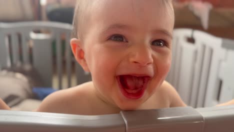 big baby laugh, with true joy of happiness, portrait of caucasian toddler standing in his playpen