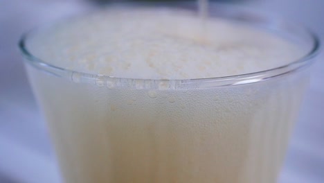 la parte superior del vaso de cerveza en primer plano a medida que se agrega más cerveza mostrando la espuma blanca aumentando en cámara lenta