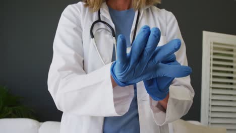 Midsection-of-caucasian-senior-female-doctor-putting-on-surgical-gloves