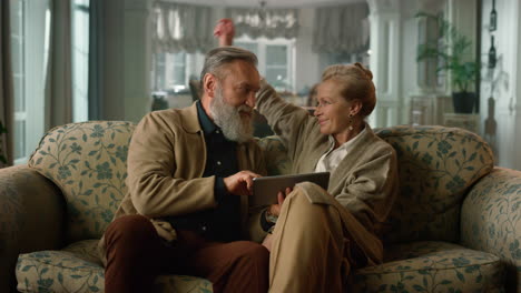 old couple looking tablet screen and hugging in the living room