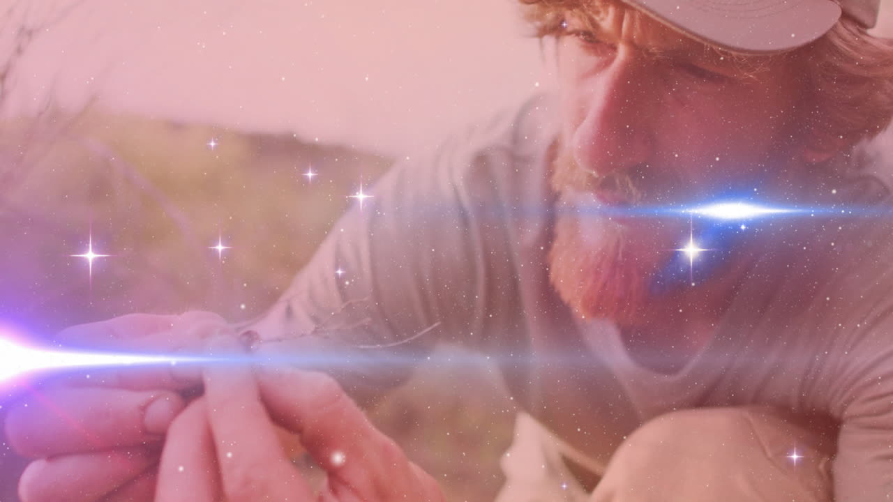 man kneeling in dry grass field, holding twig amid sparkling stars and lens flare for education