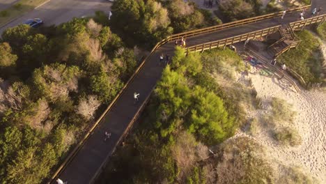 Toma-Aérea-De-Arriba-Hacia-Abajo-Niños-Montando-Bicicleta-En-El-Camino-Al-Lado-De-La-Playa-De-Vacaciones-En-Punta-Del-Este,-Uruguay