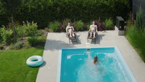 a family with a child relaxes by the small pool in their villa. parents sunbathe, child swims