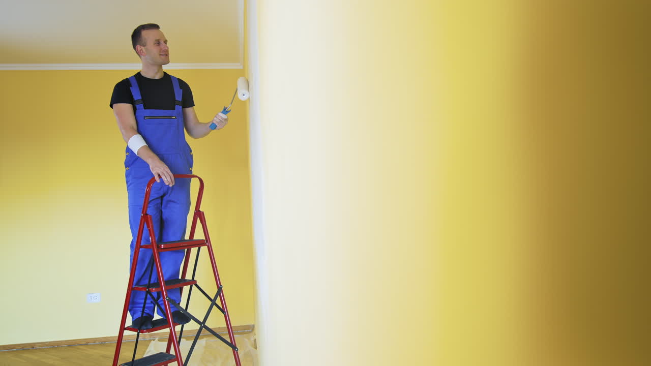 Man in working overall painting wall. Builder man painting the walls in the apartment