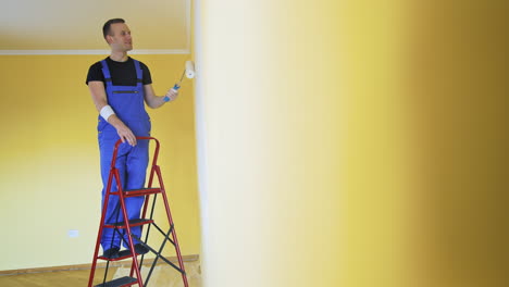 man in working overall painting wall. builder man painting the walls in the apartment