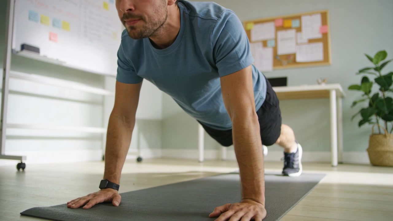 Starting plank, man lowering, pressing up on mat in home office for fitness wearing blue tee