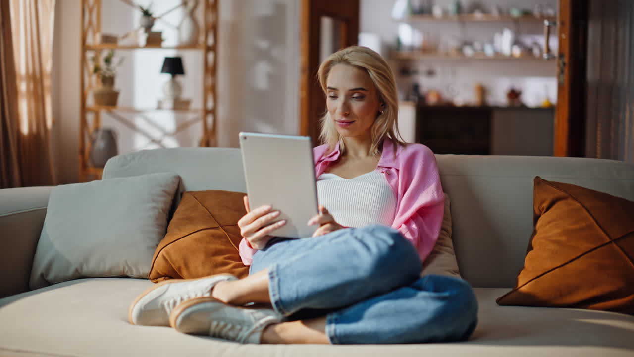 Happy woman browsing tablet screen relaxing apartment couch. Girl sitting sofa