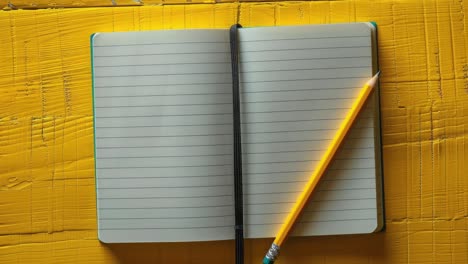 open lined notebook with pencil on yellow wooden surface