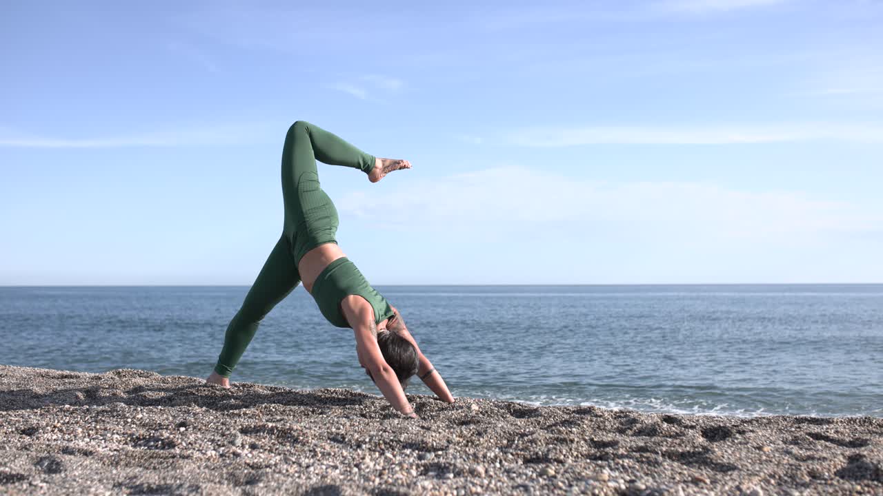 Woman performing three-legged downward-facing dog pose on beach