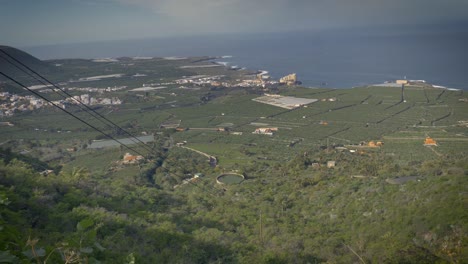 vista de la costa de tenerife desde lo alto de una exuberante ladera verde con vistas a las granjas y pueblos de abajo