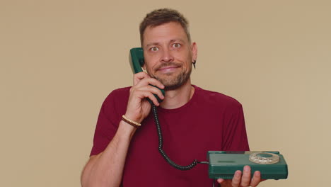 Crazy-man-in-red-t-shirt-talking-on-wired-vintage-telephone-of-80s,-fooling-making-silly-faces