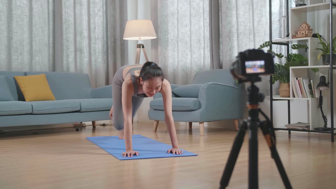 vista completa de una joven entrenadora asiática hablando a la cámara antes de hacer ejercicios de cardio rodillas altas y ejercicios de fortalecimiento del núcleo mientras graba ejercicios de enseñanza en casa