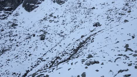 Drone-footage-passing-by-a-refuge-on-a-cliff-in-snowy-moutains-with-a-man-in-red-making-a-sign