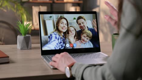 Niña-Agitando-Su-Mano-Y-Chateando-En-Video-Con-Una-Familia-Feliz-En-Una-Laptop-A-Través-De-Una-Cámara-Web