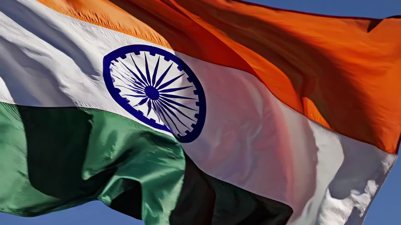 Low-angle shot of the Indian flag waving against a clear blue sky, capturing its vibrant colors