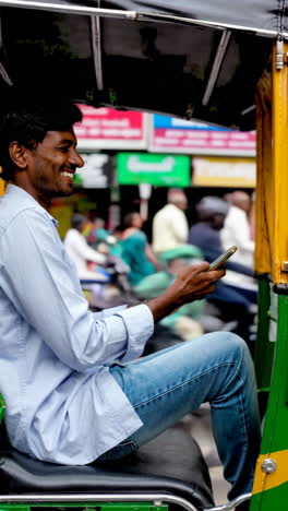 smiling indian auto-rickshaw driver using a phone on a city street