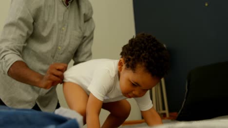 Mid-section-of-black-father-helping-his-son-changing-his-clothes-on-bed-in-a-comfortable-home-4k