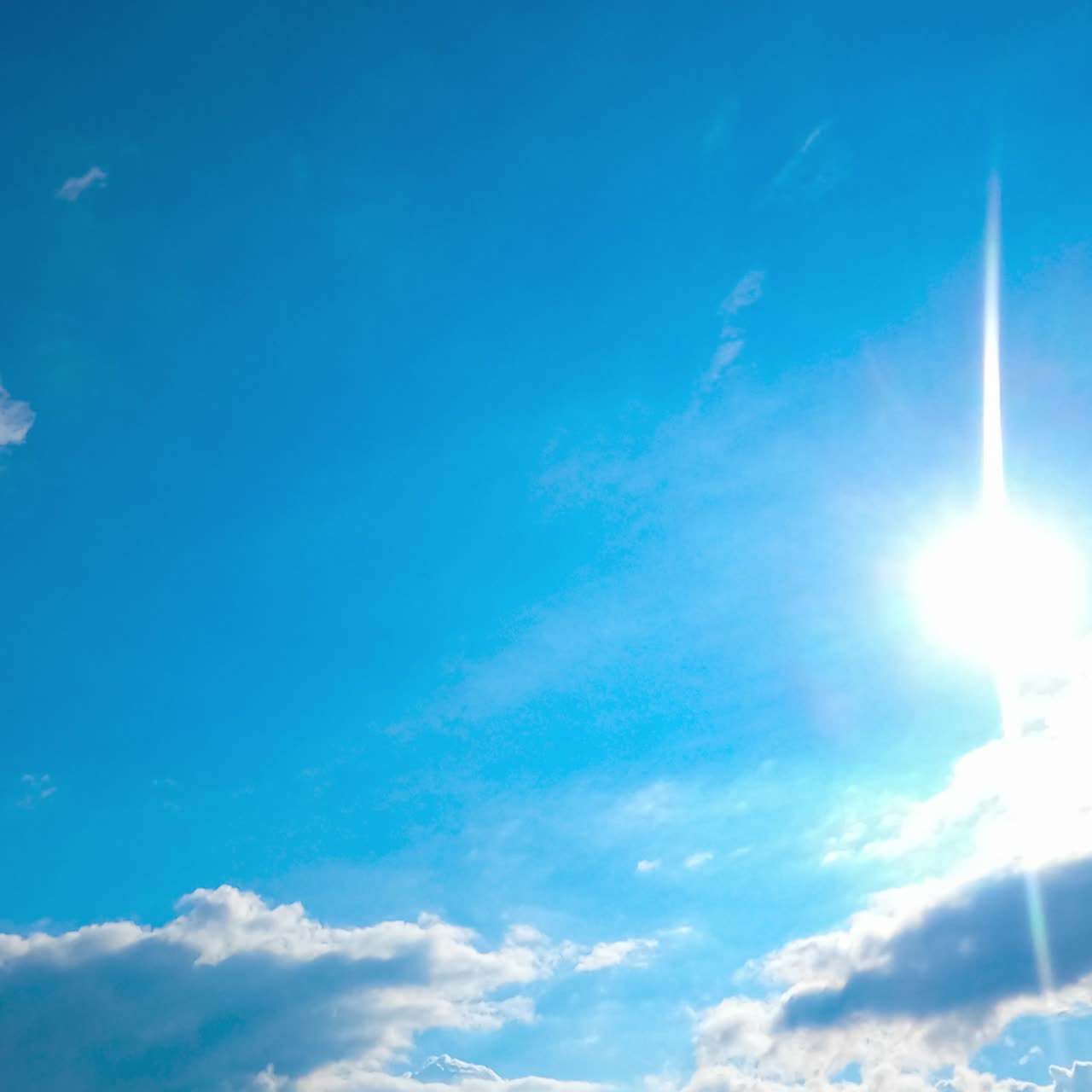 Sun beaming through the clouds moving along the bright summer sky. Skyline clears away. Timelapse